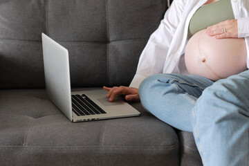 Naklejka premium Attractive pregnant young lady working remotely online from home. Close up woman hands on laptop with big belly advanced pregnancy