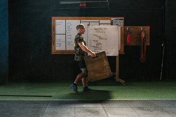 Male trainer carrying wooden box in gym