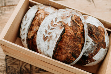 Woman holds fresh made sourdough bread in a wood crate.