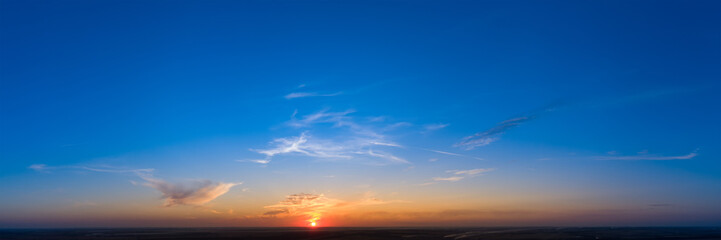 Cloudless sunrise sunset, orange light on a blue panorama background.