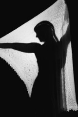 Black and white high-contrast silhouette of a girl behind a translucent scarf or plaid.