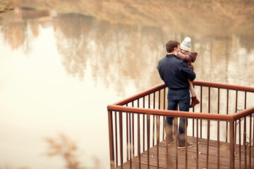 Fototapeta premium happy family walking in autumn park with lake,dad hugs and holds child, copy space, hello september
