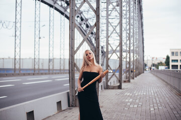 Young luxury woman with blonde hair, in black dress holding baseball bat