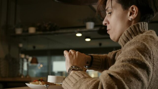 interesting girl with a short haircut appetizing eats sitting at the table in the restaurant. High quality FullHD footage