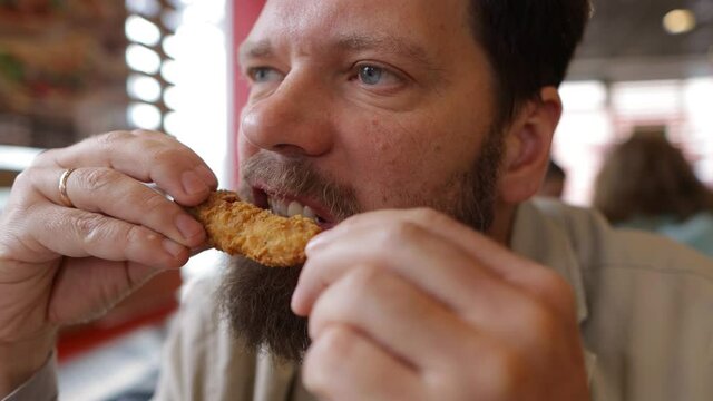 Bearded man eats fried chicken in fast food