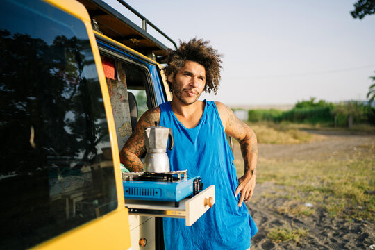 Hipster traveler relaxing near camper van with coffee in nature