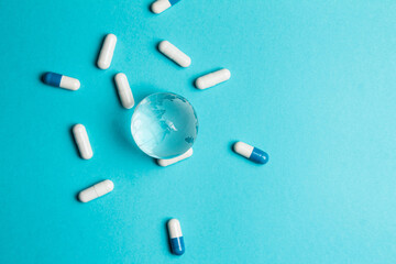 World pandemic. Glass globe Earth and capsule pill white-blue on a turquoise background. Macro top down view with copy space. A healthy nation