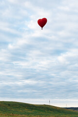 Fototapeta premium Red hot air balloon in shape of heart is landing on the green field