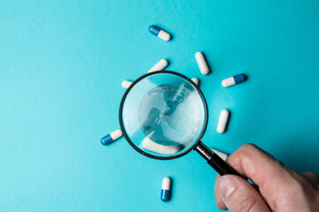 Globe and pills under magnifying glass on turquoise background. Under the supervision of healthcare. Monitoring the health of the planet Earth. People's health is under the control of doctors. Closeup