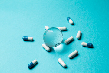 Global epidemic, pandemic concept. Glass globe Earth and capsule pill white-blue on a turquoise background. Healthy population. Closeup