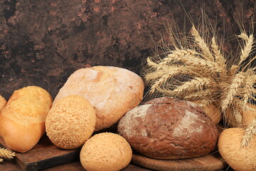 Freshly baked homemade sourdough bread with crispy crust and ears of rye and wheat on an old wooden background with place for text, modern bakery concept, healthy natural food,