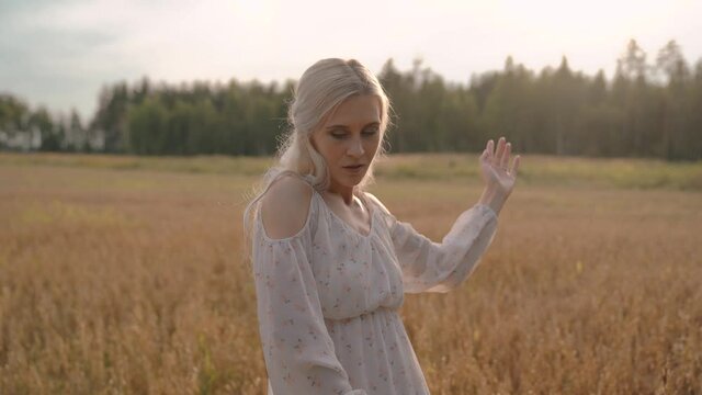 Beautiful european blonde woman waving her hands in a wheat field, posing
