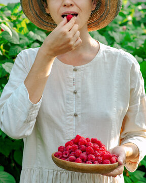 Young woman holds a plate with raspberries and eats one