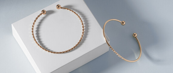 Panoramic shot of two modern golden bracelets on white box on blue background with copy space - obrazy, fototapety, plakaty