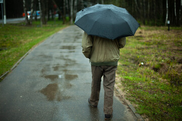 A man with an umbrella is walking down the street. Rainy autumn weather. The citizen is hiding from...