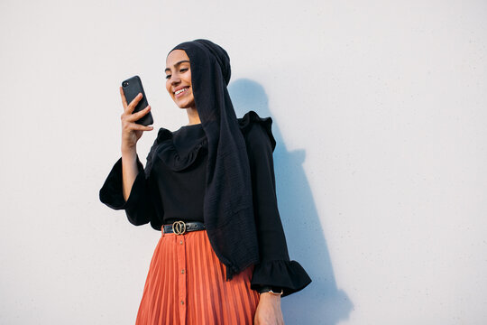 Cheerful Muslim woman in fashionable clothes talking on phone
