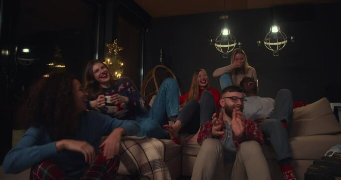 Group of happy young diverse friends watching fun movies using projector, laughing together at house party slow motion.