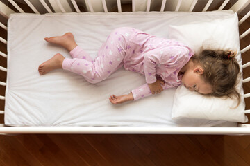 Fototapeta na wymiar top view Cute little 3-4 years preschool baby girl kid sleeping sweetly in white crib during lunch rest time in pink pajama with pillow at home. Childhood, leisure, comfort, medicine, health concept