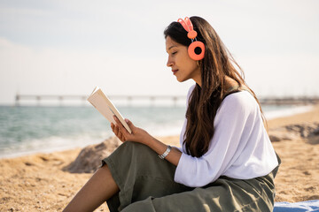 Beautiful young woman relaxing reading book at beach