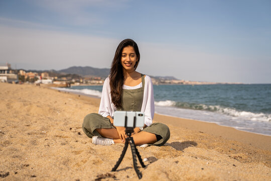 Beautiful young woman filming meditation video at beach