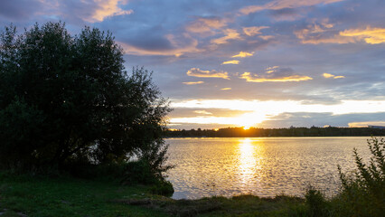 Fototapeta na wymiar Dramatic Sunset At Lake. Sunset at coast of the lake. Reflection. Blue sky and yellow sunlight. Landscape during sunset. Panoramic banner. Nature concept.