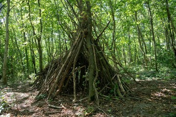 simple wooden shelter made by children in a green forest 