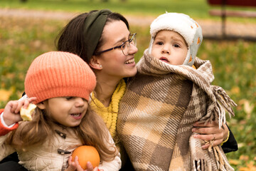 Obraz premium Young Woman Mom And Little Cute Preschool Minor Children In Orange Plaid At Yellow Fallen Leaves Nice Smiling Look At Camera In Cold Weather In Fall Park. Childhood, Family, Motherhood, Autumn Concept