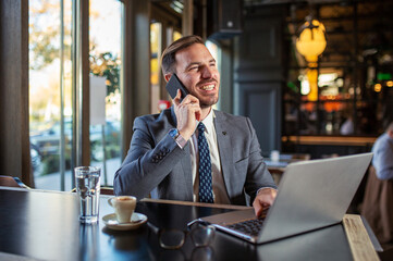 Casual businessman in cafe using laptop and talking on phone