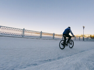 A young boy rides on the bicycle on snow cover road along the waterfront in winter