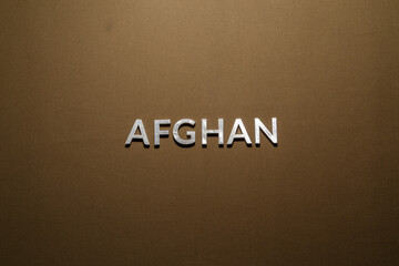 the word afghan laid with silver metal letters on rough tan khaki canvas fabric