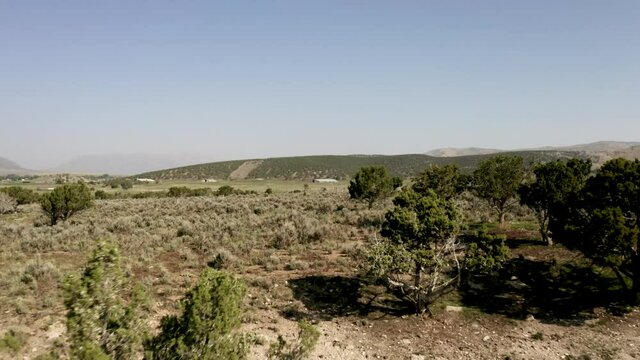 Aerial-Pulling back-View of high desert rural mountain valley back through juniper trees and sagebrush hills