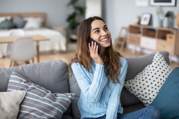 Smiling woman on a sofa in a cozy interior and talking on a smartphone