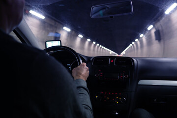 ar driver driving through a long, dark, lamp-lit tunnel in the Swiss mountains, selective focus on...