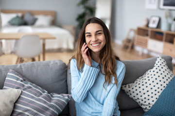 Smiling woman on a sofa in a cozy interior and talking on a smartphone
