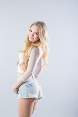 Fototapeta premium Beautiful smiling blonde in denim shorts posing on a gray.