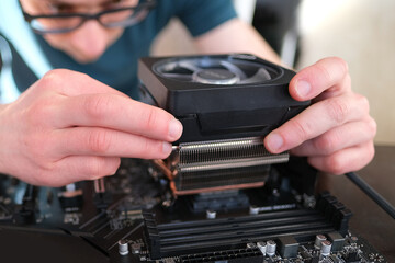 hands of young male master install cooler with copper heat pipes for the processor, other parts of...