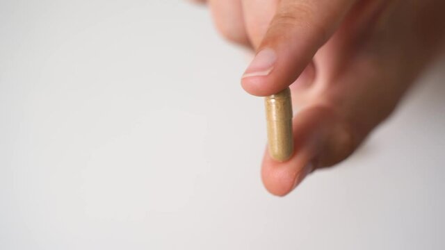 Close up hand with herb capsule on white background. Microdosing concept. Psychedelics therapy. Depression, anxiety treatment 
