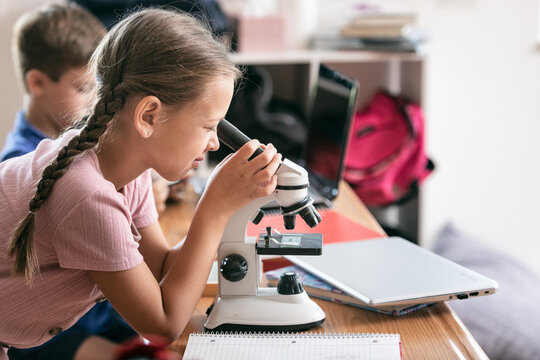 School: Female Student Using Microscope And Taking Notes