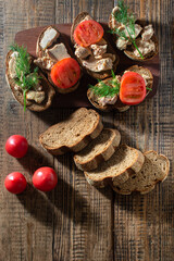 Ready-made sandwiches with cod liver, tomato and herbs lie on a wooden background, top view.