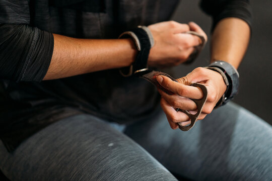 Crop sportswoman putting on barbell gloves for training