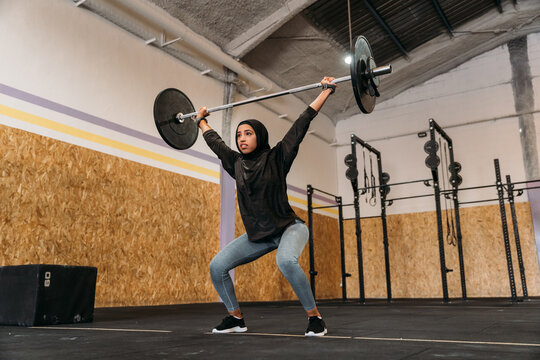 Athletic Muslim woman lifting heavy barbell