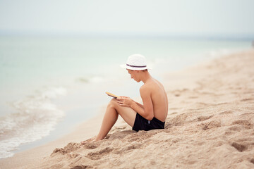 Fototapeta na wymiar A teenager reads a book on the beach. 