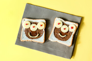 Funny monster face on halloween sandwich toast bread with peanut butter, cheese on napkin yellow background close up. Kids child sweet dessert breakfast lunch food