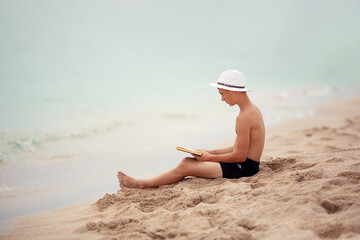 A teenager reads a book on the beach. 