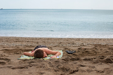 A young Caucasian male laying on a towel on a beach