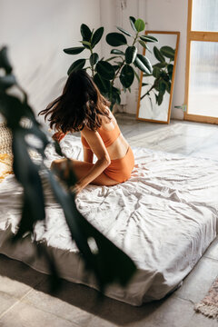A girl Sitting with her back to the camera sitting on a bed