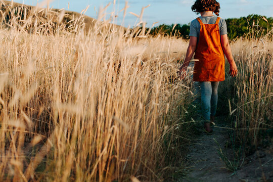 Girl walking away through field of weeds on a dirt path