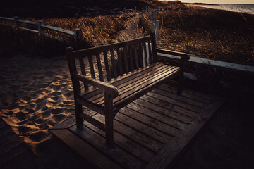 Fototapeta na wymiar Empty wooden bench on the beach after tourist hours. A dark, sulking, lonely, contemplative atmosphere of summer's end on Cape Cod.