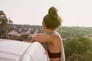 Rear view of a woman enjoying herself in a car in a field at sunset.
