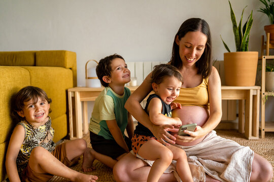 Pregnant mother using the phone with her children